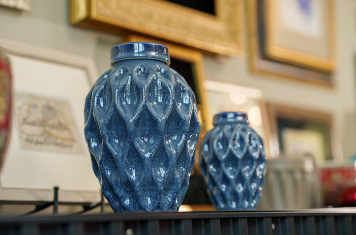 Blue glazed Echo 3D printed ceramic urn with a textured teardrop lattice surface displayed on a shelf among framed art.