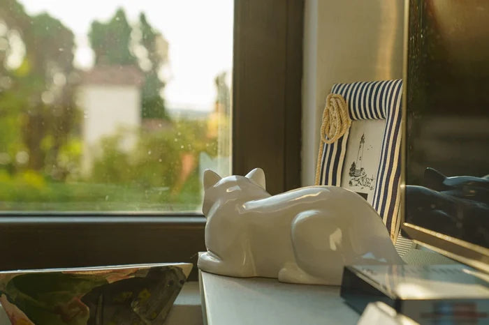 White glazed ceramic laying cat urn on a windowsill
